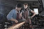 Blacksmith explaining young trainee handling of angle grinder at workshop
