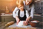 Young woman in formal clothing making dough with little adorable girl in modern kitchen.