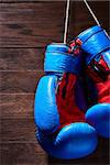 Blue and red boxing gloves hanging on wooden wall. Vertical photo of the colorful sportwear. Brown wooden background. Sportive training and exercise. Boxing backgrounds and still-life. Concept of the active lifestyle.