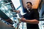 Low angle view of a young cheerful barista wearing black shirt while preparing coffee at an automatic machine in a modern coffee shop