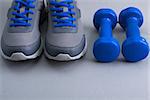 Sport equipment - gray sneakers with blue shoelaces, and blue dumbbells on gray background. Concept  healthy lifestyle, detox, diet, sport.