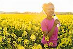 Outdoor portrait of beautiful happy mixed race African American girl teenager female young woman athlete runner drinking water from a bottle in a field of yellow flowers at sunset in golden evening sunshine
