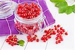 Red currants in a glass jar on a wooden white table