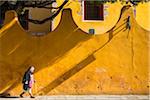 Senior woman walking with cane along street infront of yellow stucco wall in San Miguel de Allende, Mexico.