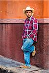 Portrait of cowboy standing on sidewalk and leaning against wall in San Miguel de Allende, Mexico