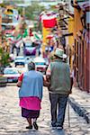 Back view of senior couple walking on cobblestone street during the St Michael Archangel Festival in San Miguel de Allende, Mexico