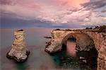 Pink sunset frames the cliffs known as Faraglioni di Sant'Andrea and the turquoise sea, province of Lecce, Apulia, Italy, Europe