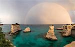 Rainbow frames rocky cliffs known as Faraglioni di Sant'andrea surrounded by turquoise sea, province of Lecce, Apulia, Italy, Europe