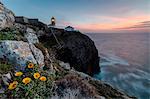 Pink sky at sunset and yellow flowers frame the lighthouse, Cabo De Sao Vicente, Sagres, Algarve, Portugal, Europe
