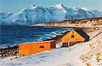 Typical wooden huts called Rorbu surrounded by waves of the cold sea and snowy peaks, Djupvik, Lyngen Alps, Troms, Norway, Scandinavia, Europe