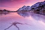 Pink sky at sunset on the frozen Lej Nair framed by snowy peaks, Bernina Pass, Canton of Graubunden, Engadine, Switzerland, Europe