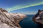 Northern Lights (aurora borealis) on the snowy peaks and the village of Fjordgard framed by the frozen sea, Ornfjorden, Senja, Troms, Norway, Scandinavia, Europe