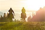 Two cowboys riding on horseback in a Prairie landscape at sunset.