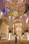 Man standing underneath white and golden dome of Sheikh Zayed Mosque, Abu Dhabi, United Arab Emirates.