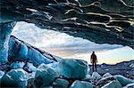 Rear view silhouette of person standing on ice rock at the entrance to a glacial ice cave.