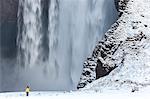 Winter landscape with rear view of person standing next to a tall waterfall.