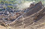 High angle view of town with man climbing up dusty mountain slope.