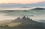 Sunrise across a misty Italian landscape of rolling hills and cypress trees, farmhouse in the distance.