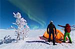 Hikers outside tent look at the Northern Lights (Aurora Borealis), Abisko, Kiruna Municipality, Norrbotten County, Lapland, Sweden, Scandinavia, Europe