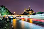Long exposure of a boat on the River Seine passing Notre Dame Cathedral on a wet evening in Paris, France, Europe