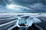 Glacier ice on black sand beach with waves washing up the beach on a stormy winter day, near Jokulsarlon, South Iceland, Polar Regions