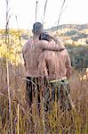 Rear view of two bare chested men looking out at landscape from long grass, Guaramiranga, Ceara, Brazil