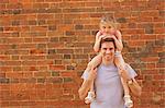 Portrait of mid adult man carrying daughter on shoulders by brick wall