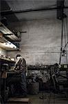 Mechanic working at bench with dismantled vintage motorcycle in workshop