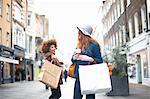 Two young women, holding shopping bags, passing each other in street