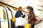 Two young women standing on underground train platform, holding shopping bags