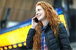 Young woman at train station, talking on smartphone