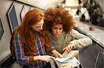 Two young women on escalator, looking at map, elevated view