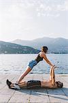 Young woman balancing with boyfriend lying on waterfront, Lake Como, Lombardy, Italy
