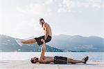 Young man lying on back supporting friend on waterfront, Lake Como, Lombardy, Italy