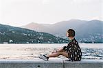 Young woman sitting on waterfront wall at Lake Como, Lombardy, Italy