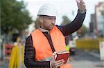 Road engineer signalling with hand and holding digital tablet
