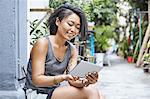 Woman sitting on doorstep in residential alleyway looking at digital tablet, Shanghai French Concession, Shanghai, China