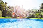 Father and sons in mid air jumping into outdoor swimming pool