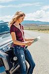 Woman leaning against car looking at map