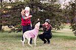 Girl and her sister playing with dog in garden