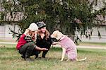 Girl and her sister crouching to hold dog's paw in garden