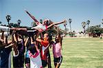 Schoolgirl soccer team carrying player above their heads on school sports field