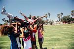 Schoolgirl soccer team carrying player above their heads on school sports field