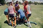 Schoolgirl soccer team tending injured player on school sports field