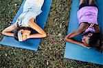 Overhead view of two schoolgirls lying on yoga mats on school sports field