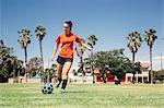 Teenage schoolgirl kicking soccer ball on school sports field