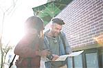 Man and woman outdoors, man looking at map, woman holding camera