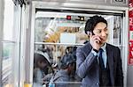 Businessman wearing suit standing on a commuter train, talking on mobile phone.