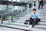 Businessman wearing blue shirt sitting outdoors on steps, looking at mobile phone.