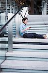 Businessman wearing blue shirt sitting outdoors on steps, holding mobile phone.